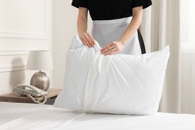 Photo of Young maid making bed in hotel room, closeup