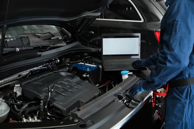Photo of Technician checking car with laptop at automobile repair shop