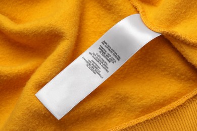 Clothing label with recommendations for care on orange garment, closeup