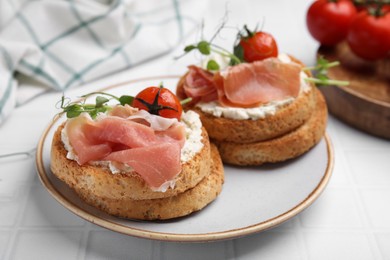 Photo of Tasty rusks with prosciutto, cream cheese and tomatoes served on white table, closeup