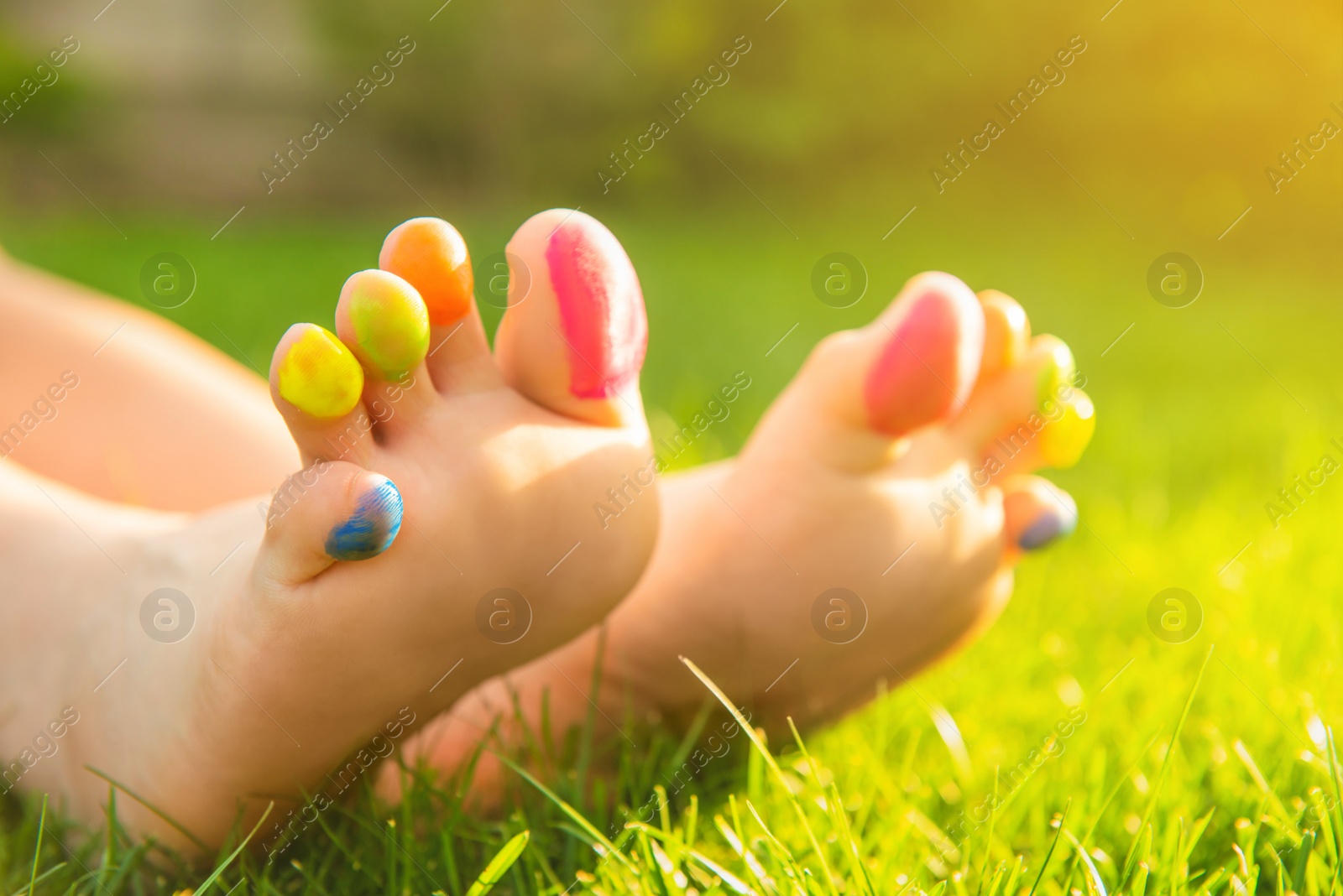 Photo of Teenage girl with painted toes on green grass outdoors, closeup