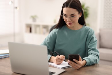 Photo of Young woman watching webinar at table in room