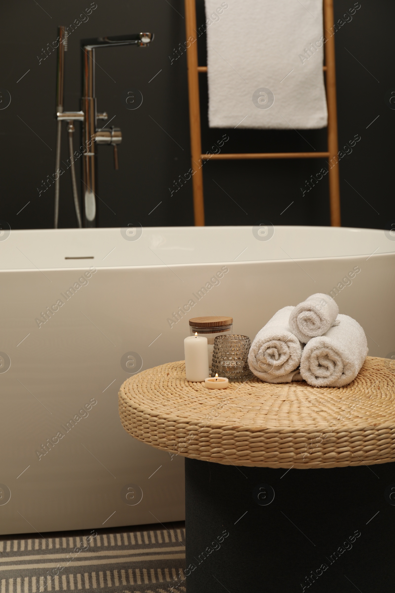 Photo of Spa day. Towels and candles on wicker table near tub in bathroom