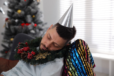 Drunk man with festive cap and wreath sleeping in room after New Year party