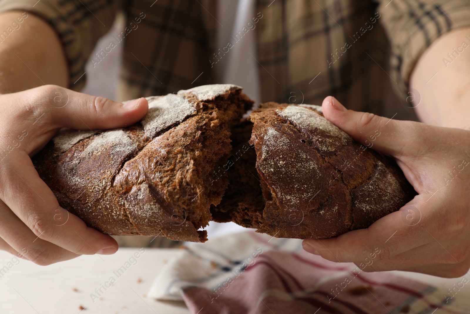 Photo of Man breaking loaf of fresh bread on white table, closeup