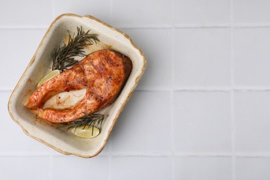 Photo of Freshly cooked fish, rosemary and lime on white tiled table, top view. Space for text