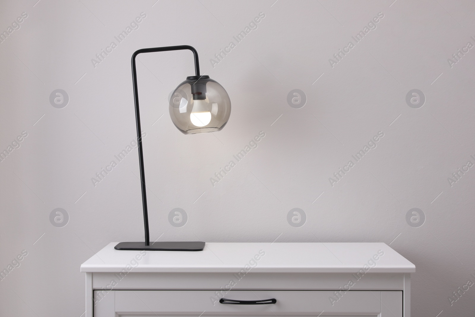 Photo of Wooden chest of drawers with lamp near white wall in room, space for text