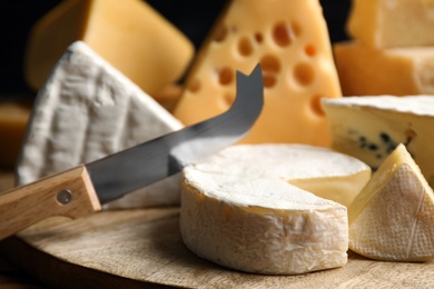 Photo of Different sorts of cheese and knife on wooden board, closeup
