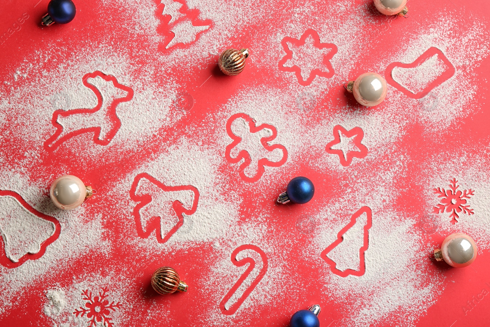 Photo of Cookie shapes made of flour and Christmas balls on red background, flat lay