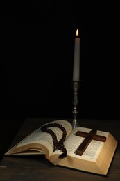 Photo of Church candle, Bible, rosary beads and cross on wooden table against black background