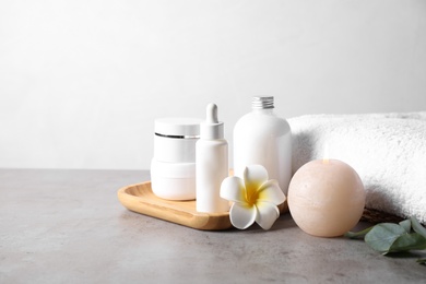 Towel, burning candle and bottles with cosmetic products on grey table