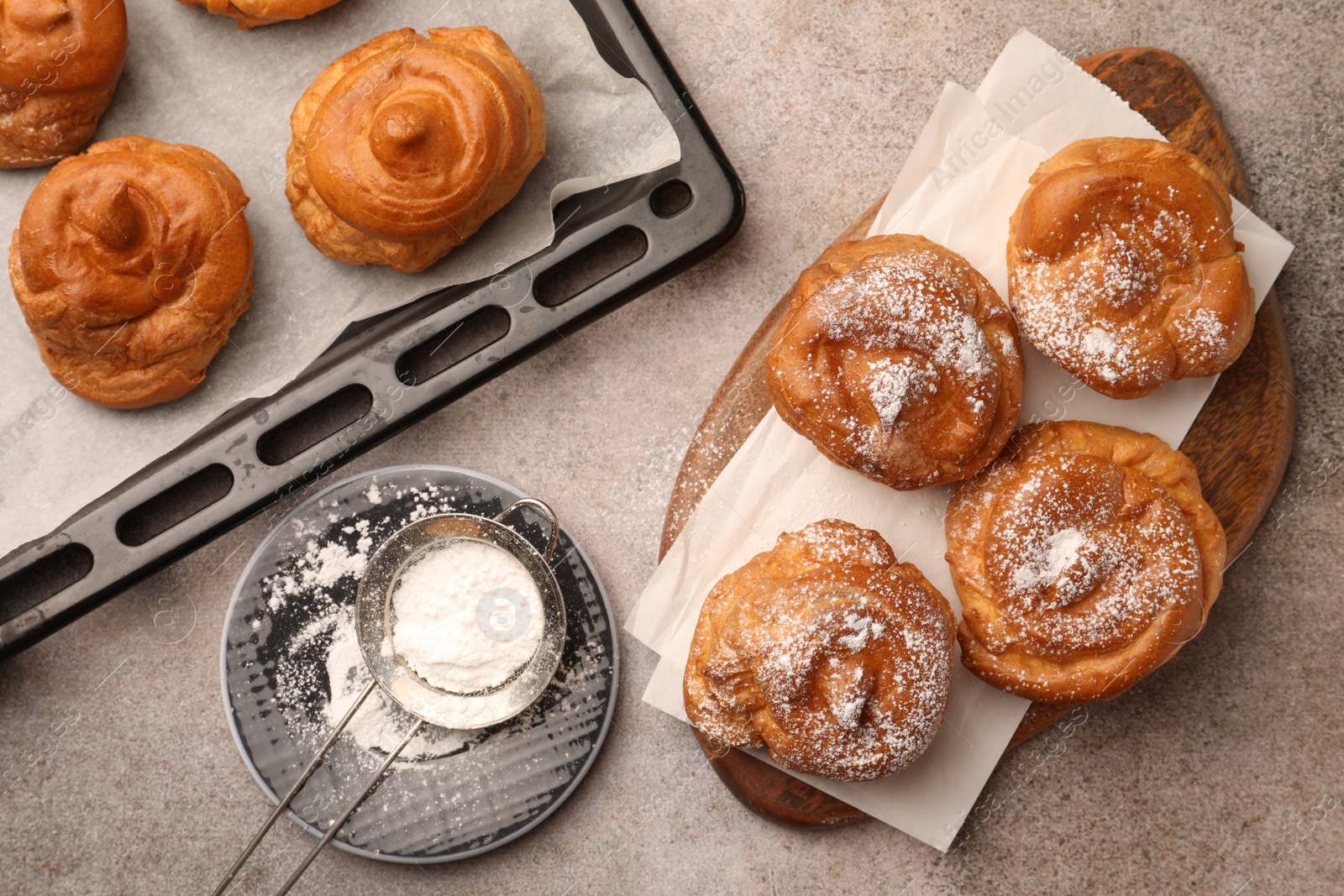 Photo of Delicious profiteroles with powdered sugar on grey table, flat lay