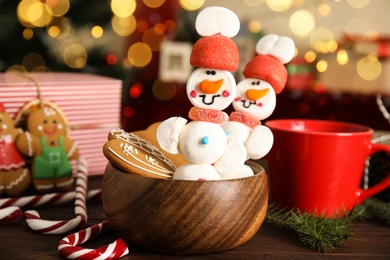 Funny snowmen made of marshmallows on wooden table against blurred festive lights
