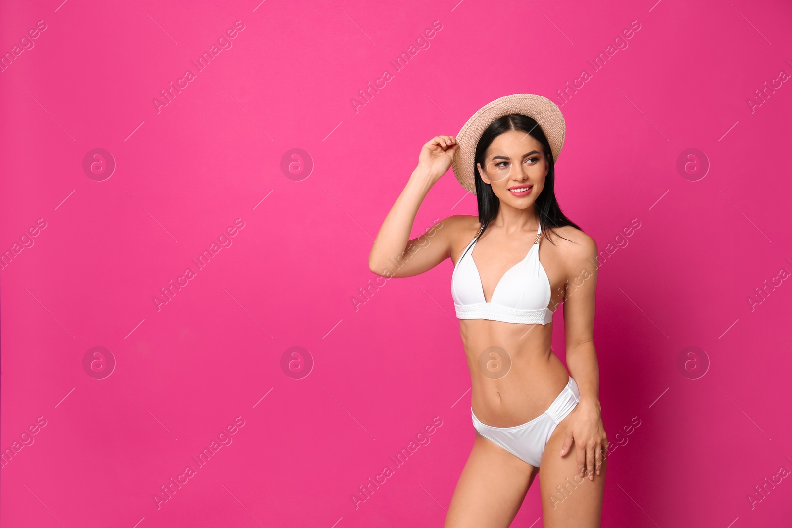 Photo of Beautiful young woman in white bikini with hat on pink background. Space for text