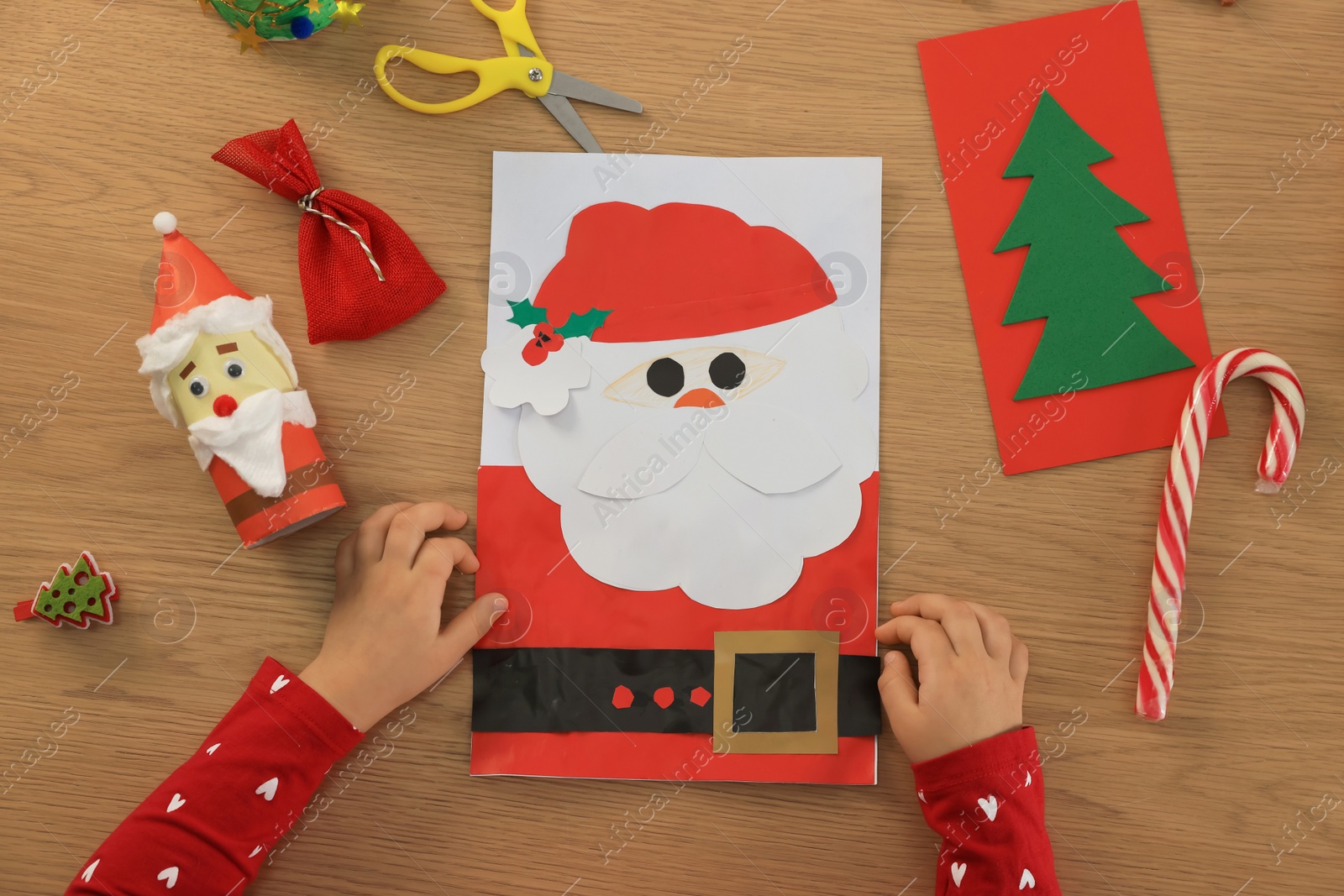 Photo of Little child with beautiful Christmas greeting card at wooden table, top view