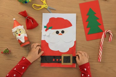 Little child with beautiful Christmas greeting card at wooden table, top view