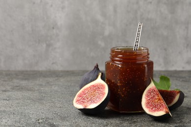 Photo of Glass jar with tasty sweet jam and fresh figs on grey textured table, space for text
