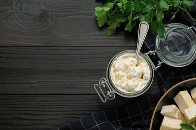 Photo of Delicious tofu cream cheese and parsley on black wooden table, flat lay. Space for text