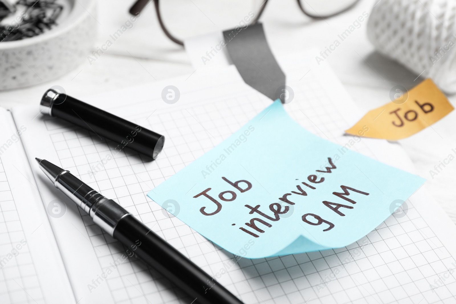 Photo of Reminder note about job interview and stationery on table, closeup