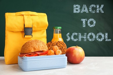 Lunch box with appetizing food and bag on table near chalkboard