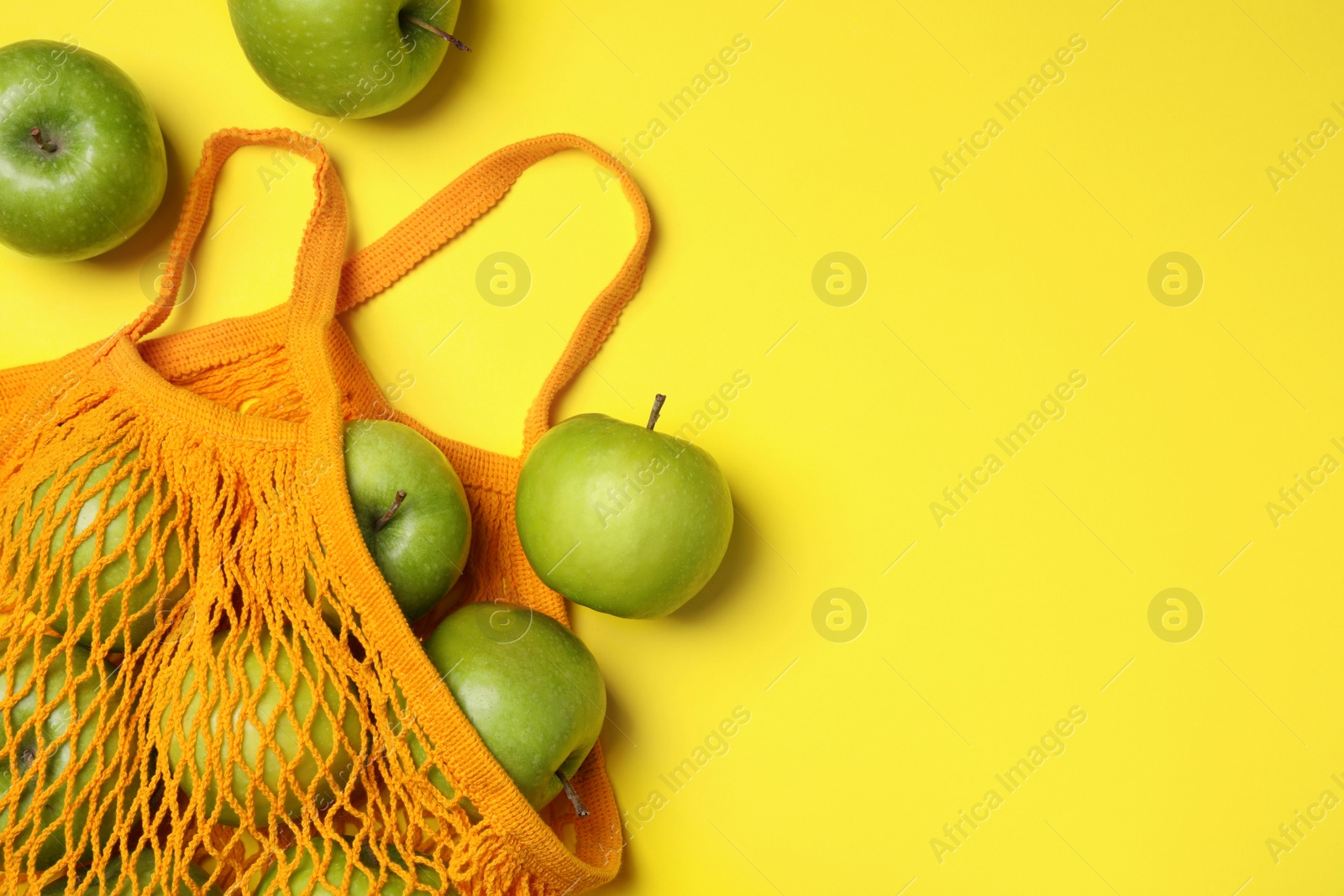 Photo of Mesh bag with ripe apples on yellow background, flat lay. Space for text