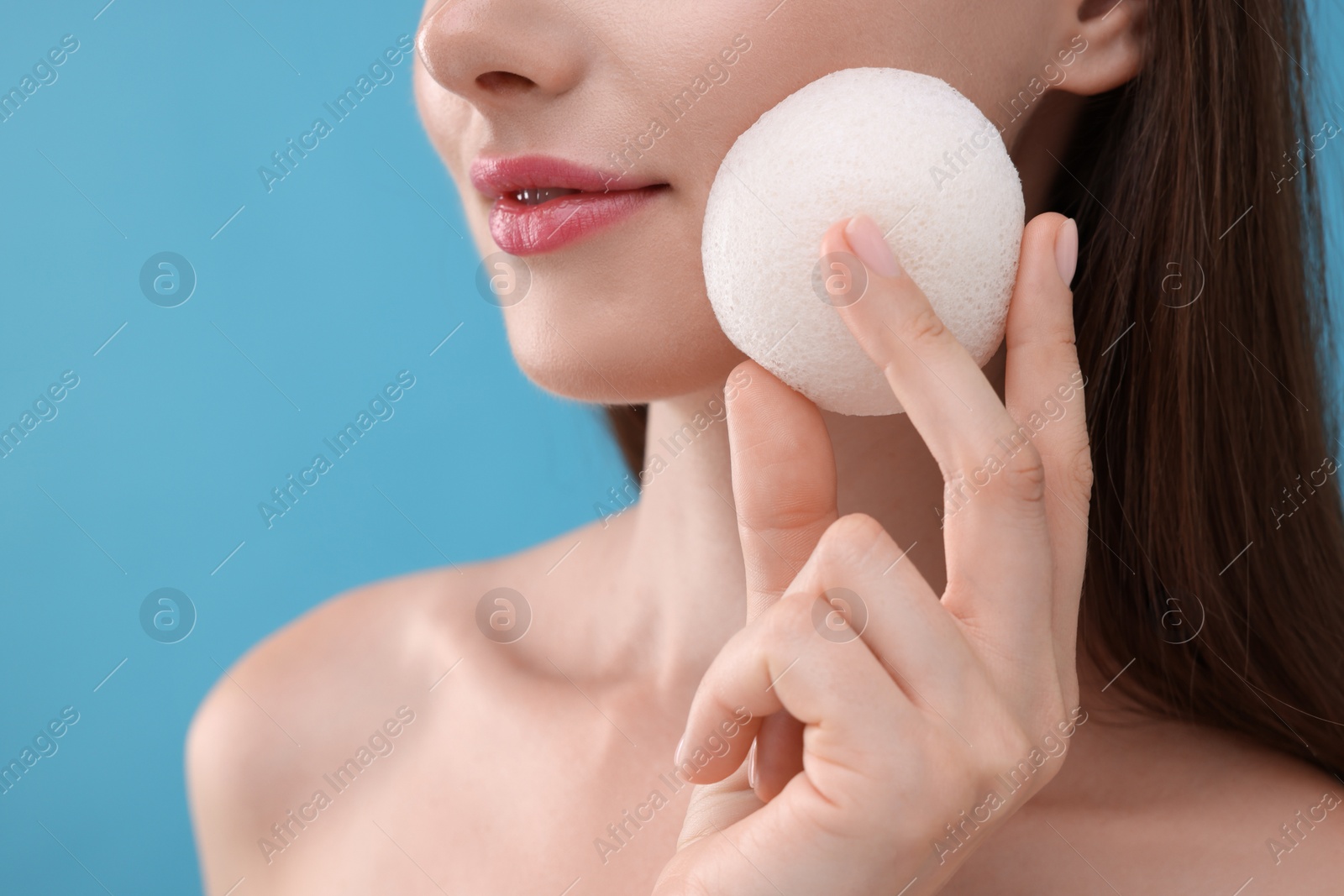 Photo of Young woman holding face sponge on light blue background, closeup