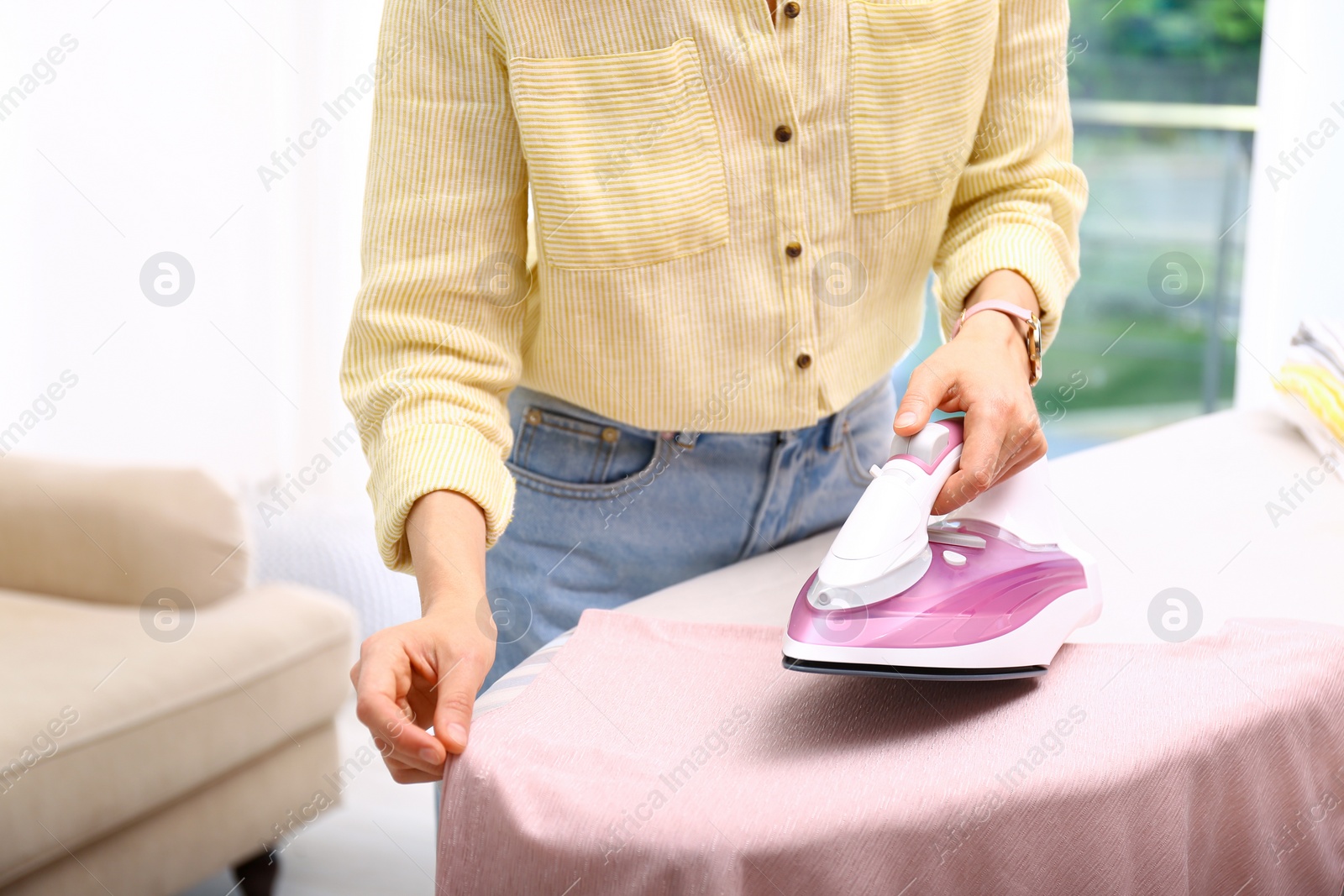 Photo of Young woman ironing clean laundry indoors, closeup