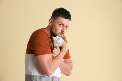 Greedy man hiding money on beige background. Space for text