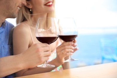 Photo of Young romantic couple with glasses of red wine at table