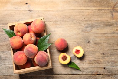 Photo of Cut and whole fresh ripe peaches with green leaves in crate on wooden table, flat lay. Space for text