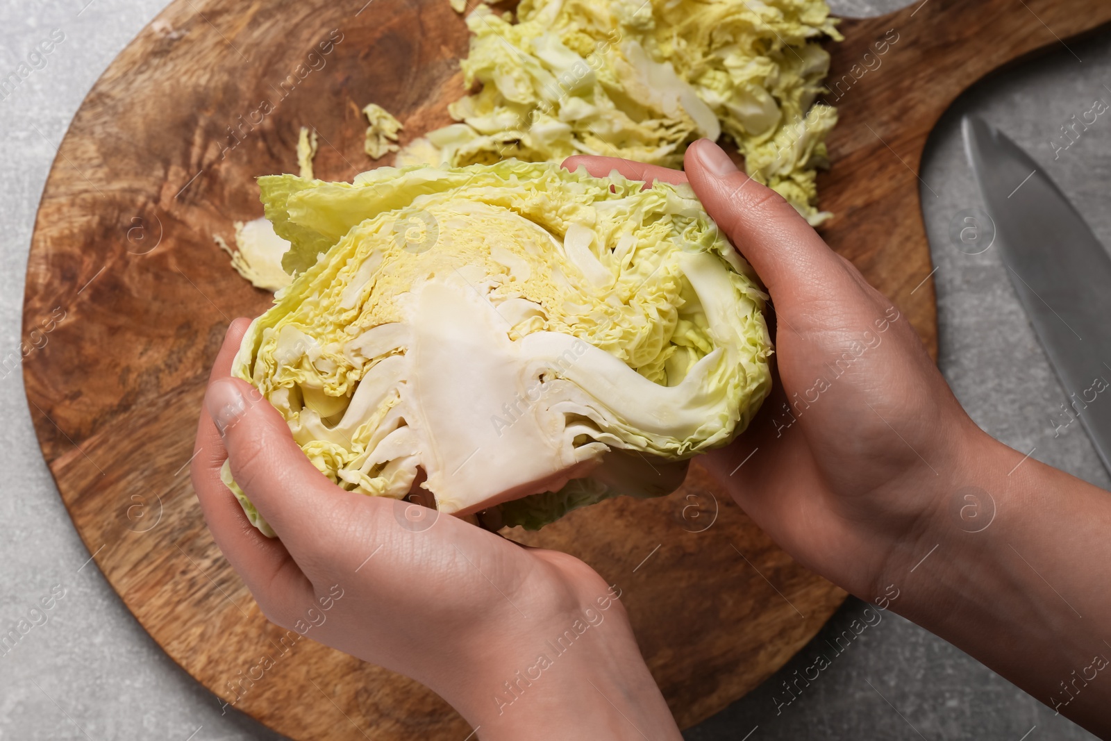 Photo of Woman holding fresh ripe cabbage above grey table, top view