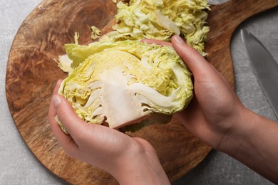 Woman holding fresh ripe cabbage above grey table, top view