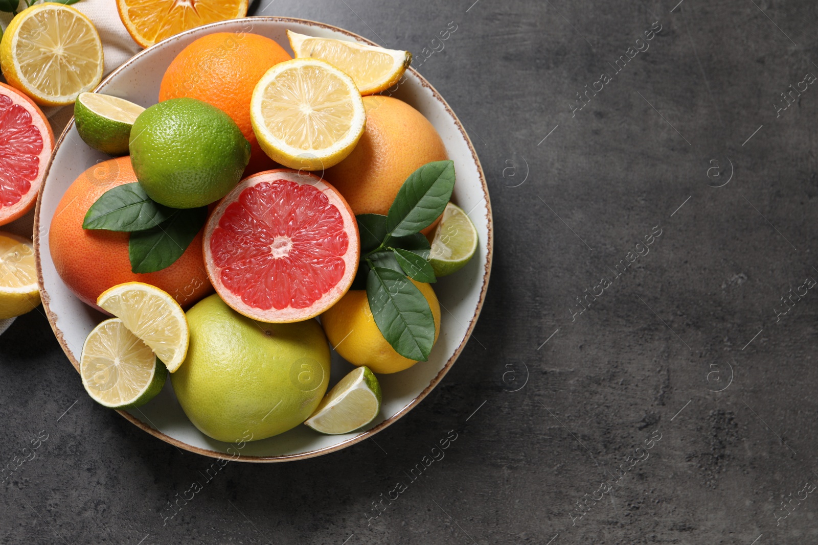 Photo of Different fresh citrus fruits and leaves on grey textured table, top view. Space for text