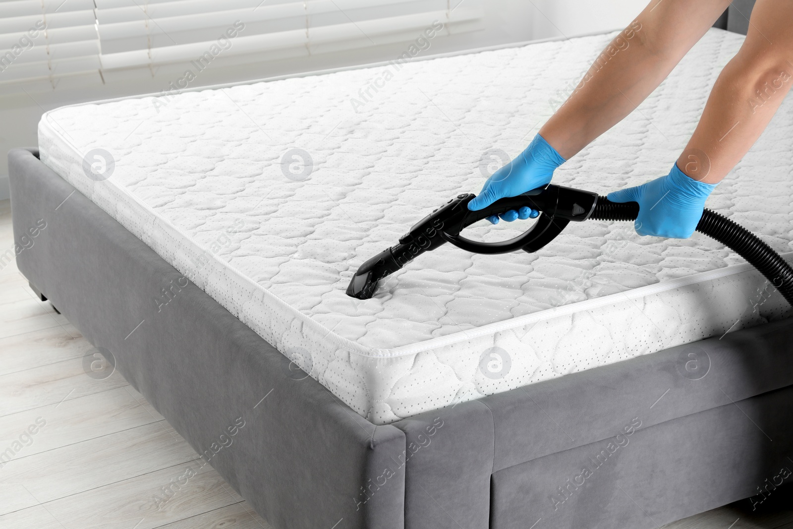 Photo of Woman disinfecting mattress with vacuum cleaner indoors, closeup