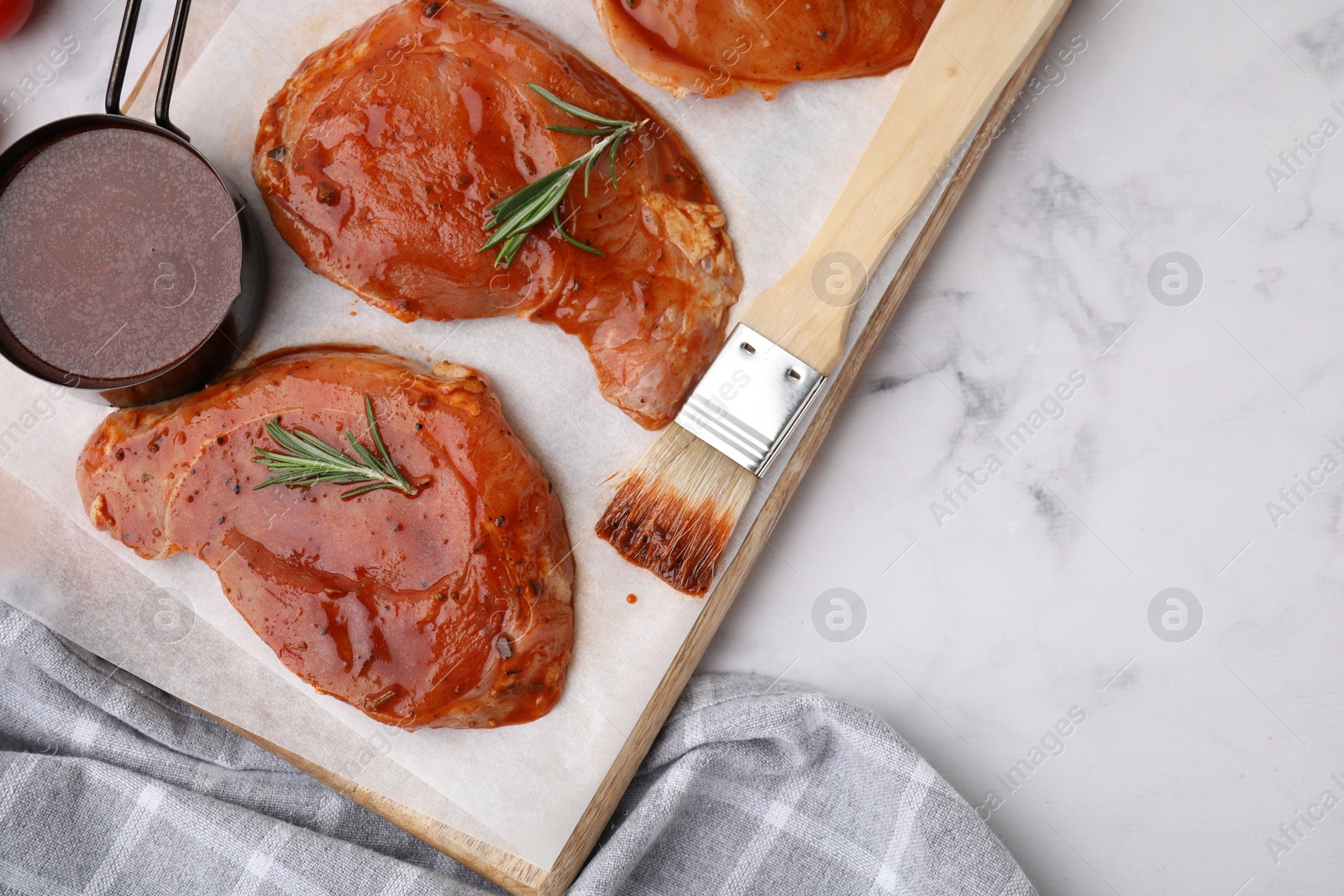 Photo of Raw marinated meat, rosemary and basting brush on white marble table, top view. Space for text
