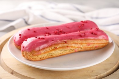 Photo of Plate with tasty glazed eclairs on wooden board, closeup