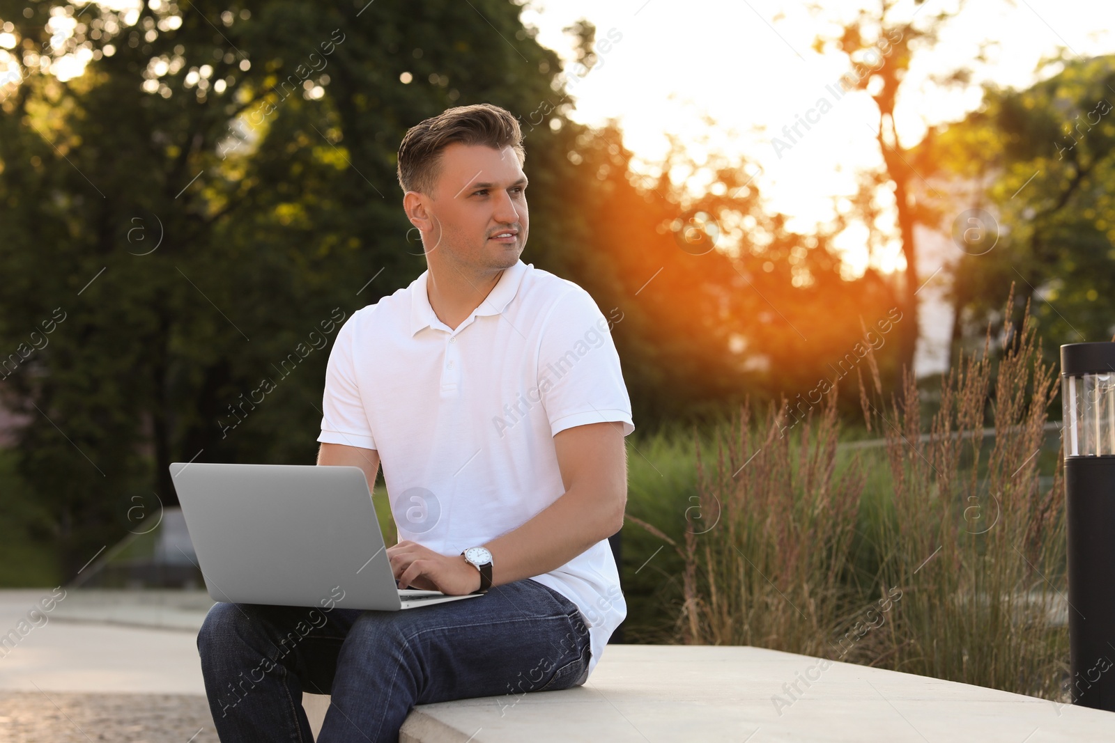 Photo of Handsome man using laptop on stone bench outdoors. Space for text