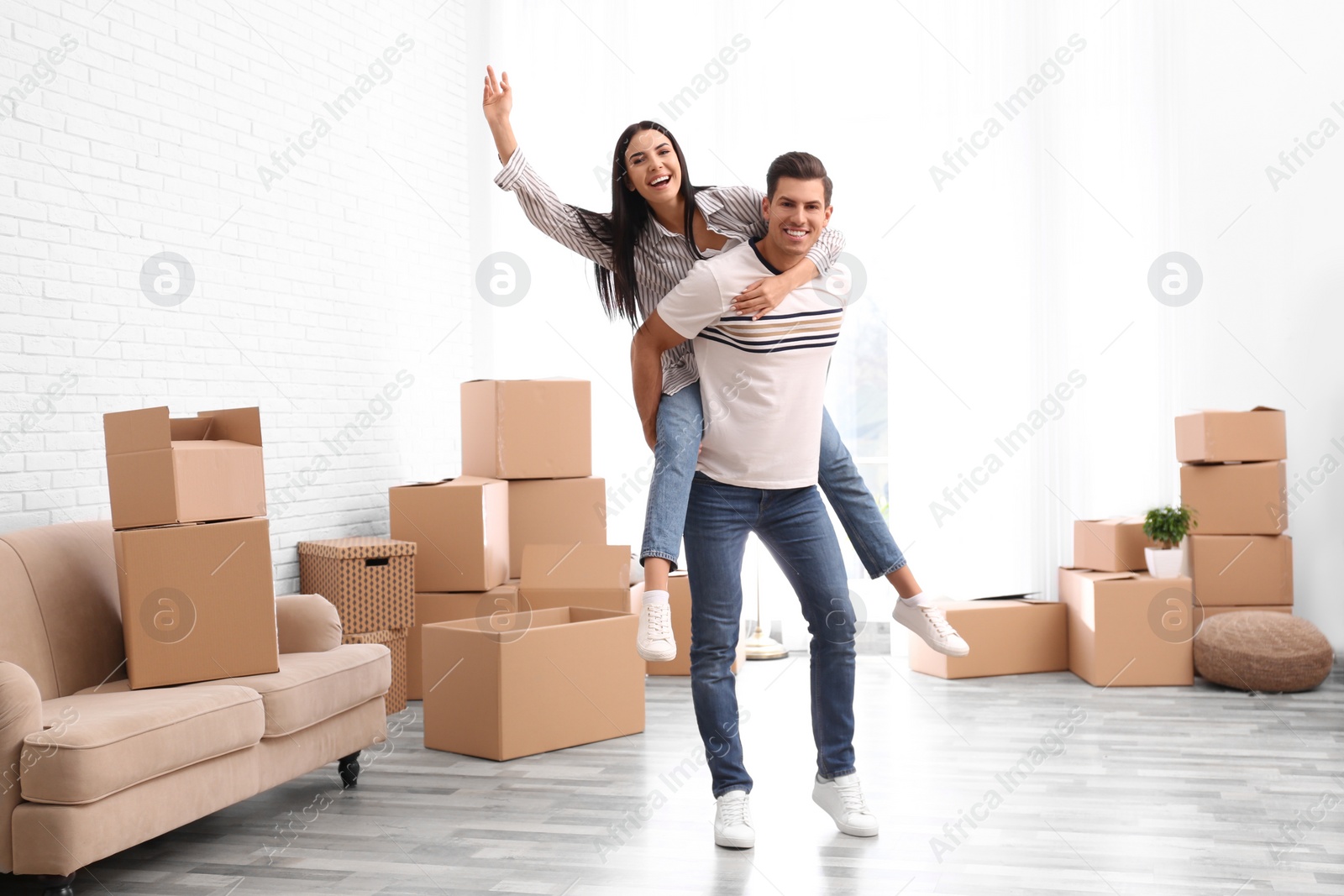 Photo of Happy couple having fun in room with cardboard boxes on moving day