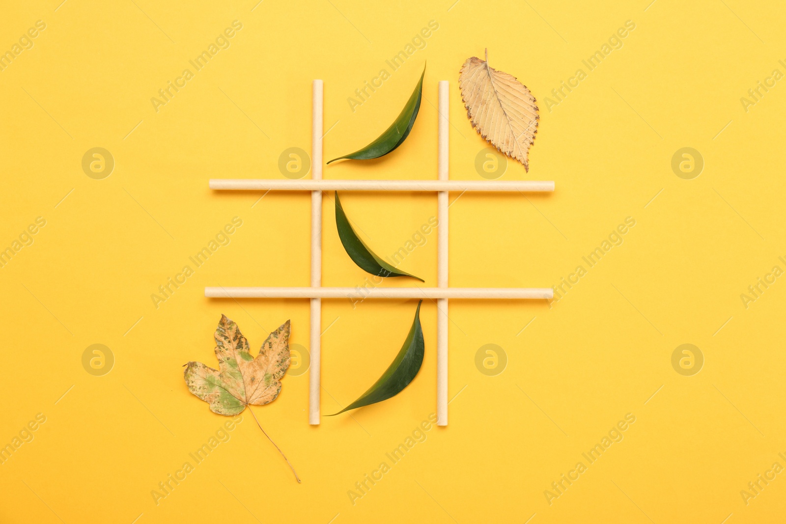 Photo of Tic tac toe game made with fresh and dry leaves on yellow background, top view