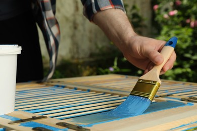 Photo of Man painting wooden surface with blue dye outdoors, closeup