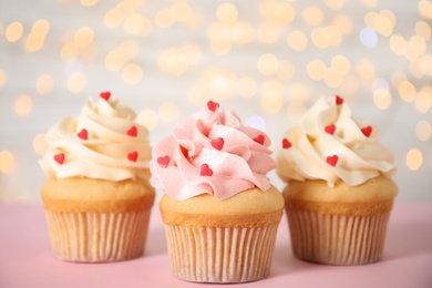 Photo of Tasty cupcakes for Valentine's Day on pink table against blurred lights