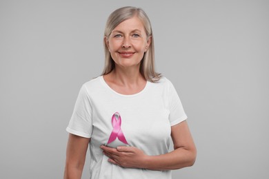Beautiful senior woman with pink ribbon on light grey background. Breast cancer awareness