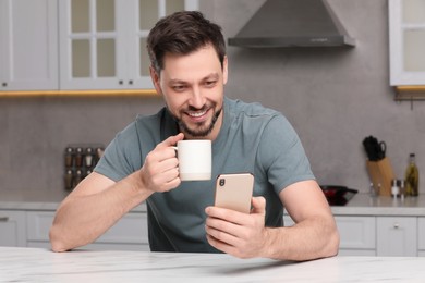 Photo of Man using smartphone while having breakfast at table in kitchen. Internet addiction