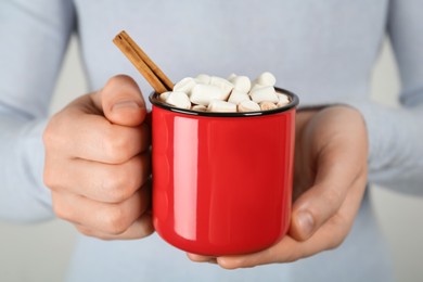 Woman holding cup of delicious hot chocolate with marshmallows and cinnamon stick, closeup