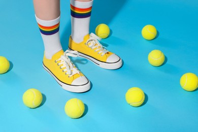 Photo of Woman wearing yellow classic old school sneakers and tennis balls on light blue background, closeup