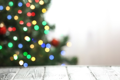 Photo of Blurred view of fir tree with glowing Christmas lights near table indoors. Festive mood