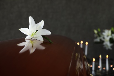 Wooden casket with white lily in funeral home, closeup. Space for text