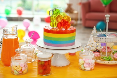 Photo of Bright birthday cake and other treats on table in decorated room