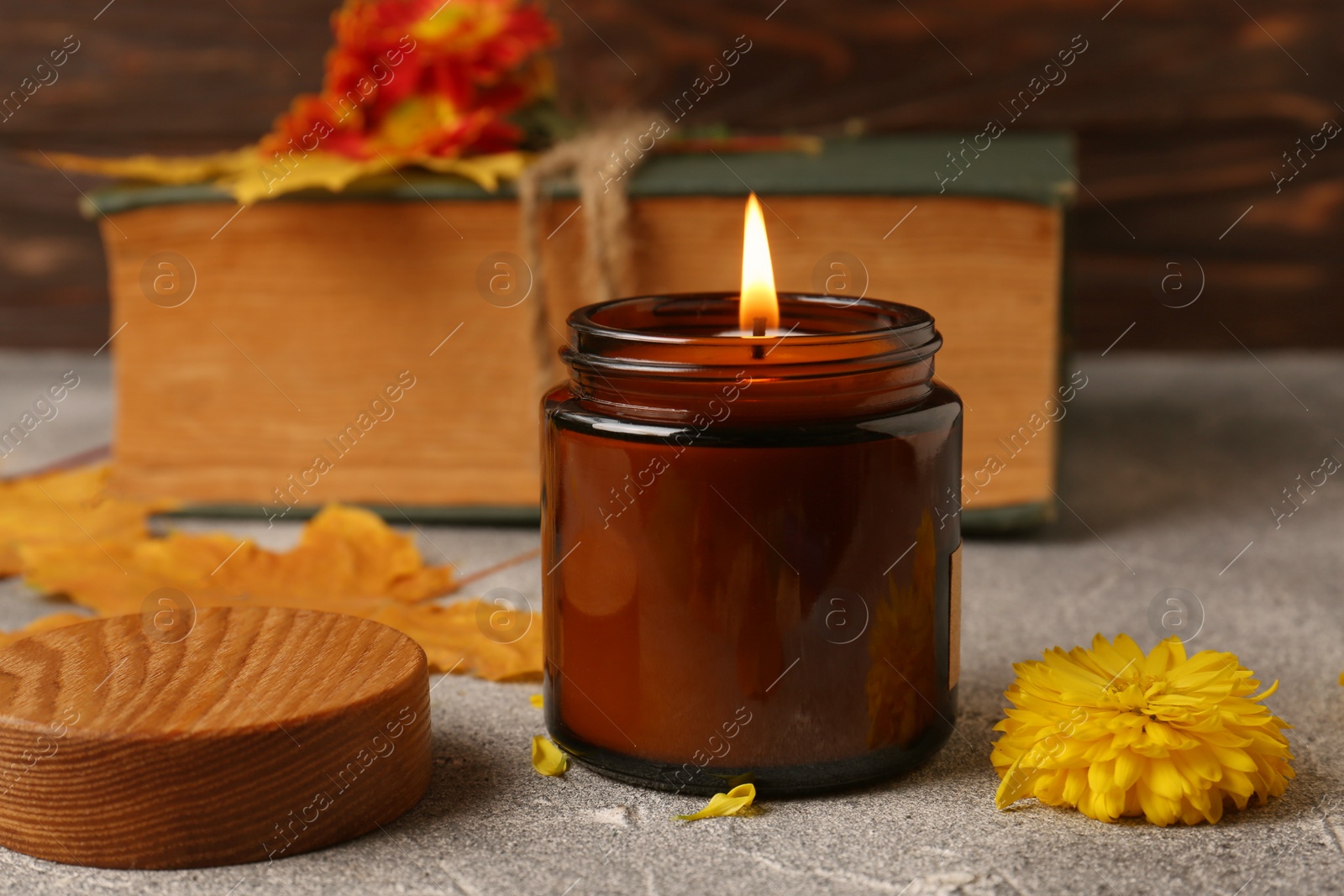 Photo of Burning scented candle, yellow flower on light gray textured table