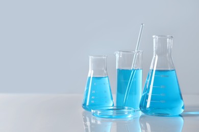 Photo of Different laboratory glassware with light blue liquid on table, space for text